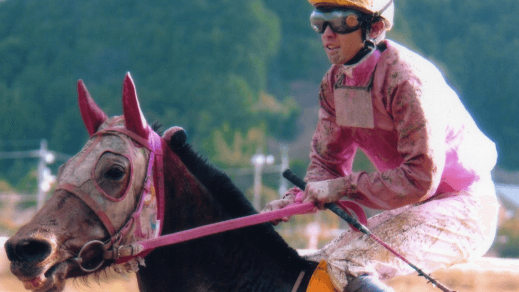 A picture of premier jockey Yutaka Take dressed in a pink shirt while riding on celebrated racehorse Haru Urara