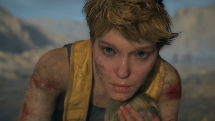 Death Stranding 2 On The Beach Fragile holding Lou with a tired expression looking at something offscreen, mountainous environment and a gray-blue sky