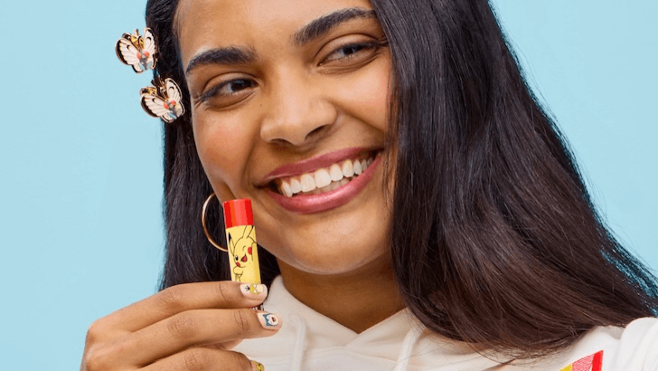 Close-up of Sydeon holding a Pikachu-themed lip balm, wearing butterfly hair clips and with nail art