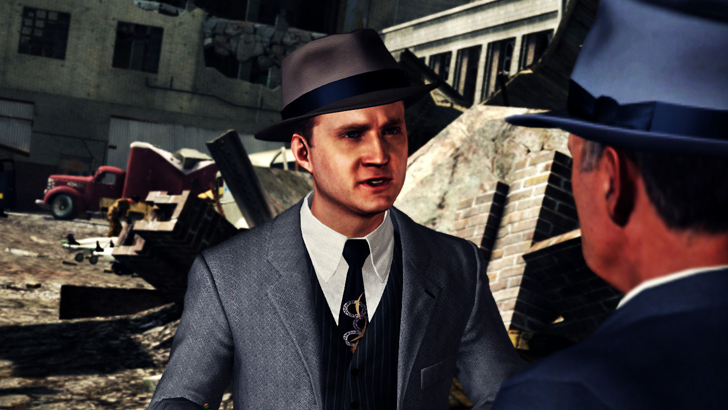 Cole Phelps in suit talking to man in suit and hat with building ruins in the background