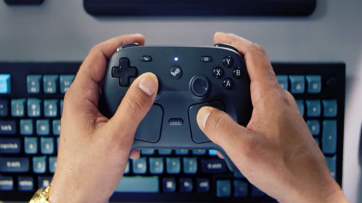 Player holds a Steam Controller in front of a keyboard and monitor setup